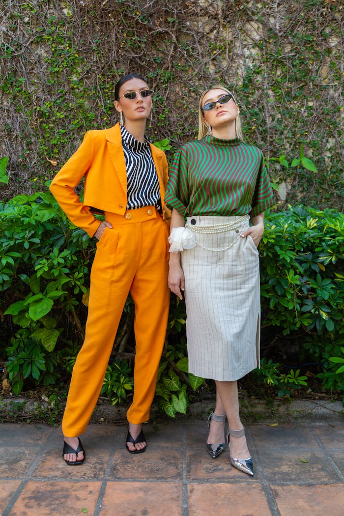 Two fashionable women posing in stylish outfits outdoors with sunglasses.