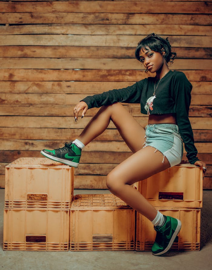 A fashionable young woman poses confidently against a wooden backdrop, showcasing modern casual style.